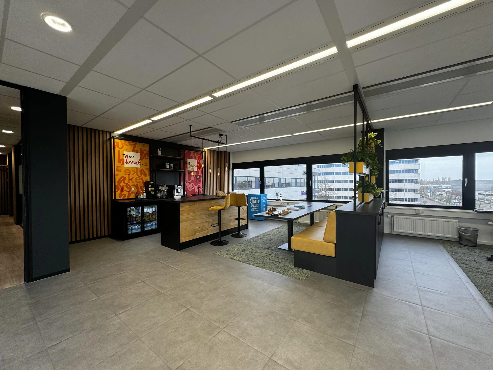 Moderne kantoorruimte in Rijnzathe met koffiecorner, zitgedeelte en uitzicht op kantoorgebouwen.