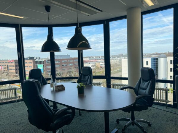 Vergaderruimte met vier zwarte stoelen, een ovale tafel en uitzicht op kantoorpanden in Rijnzathe.