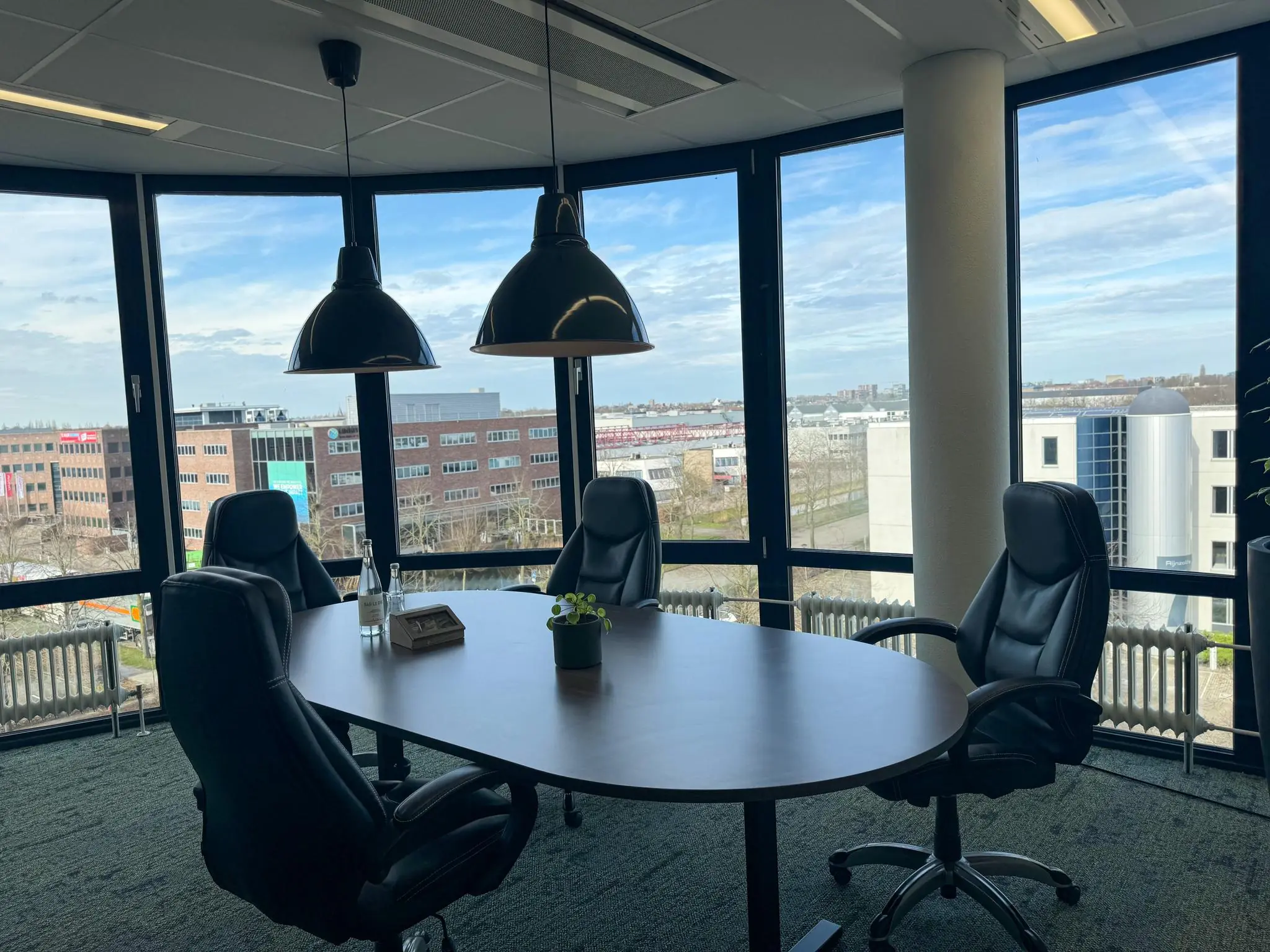 Vergaderruimte met vier zwarte stoelen, een ovale tafel en uitzicht op kantoorpanden in Rijnzathe.