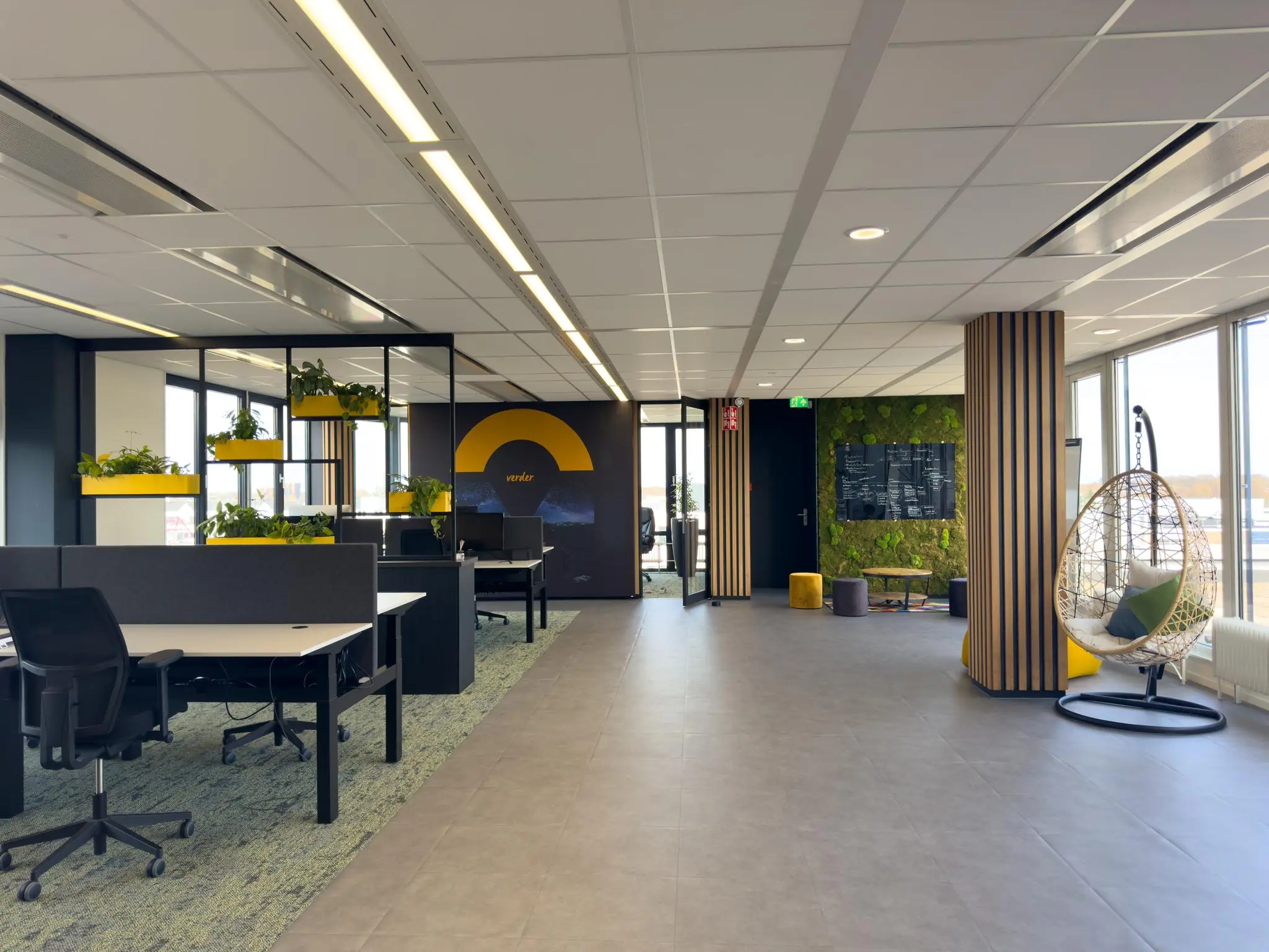 Modern kantoorinterieur in Rijnzathe met open werkplekken, planten, een moswand en een hangstoel bij het raam.