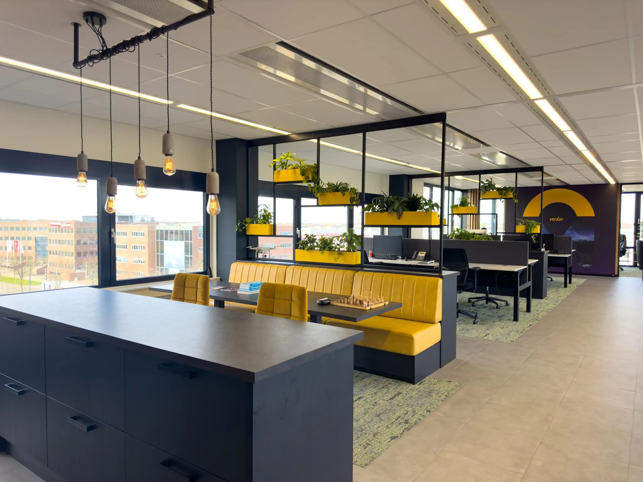 Modern kantoorinterieur aan de Rijnzathe met gele zitbanken, bureaus, hanglampen en veel groene planten.