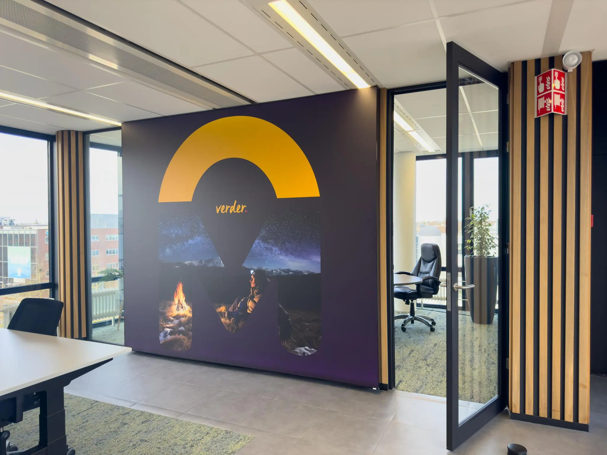 Moderne kantoorruimte met een grote wanddecoratie waarop het woord "verder." en een landschap met kampvuur en sterrenhemel te zien zijn.