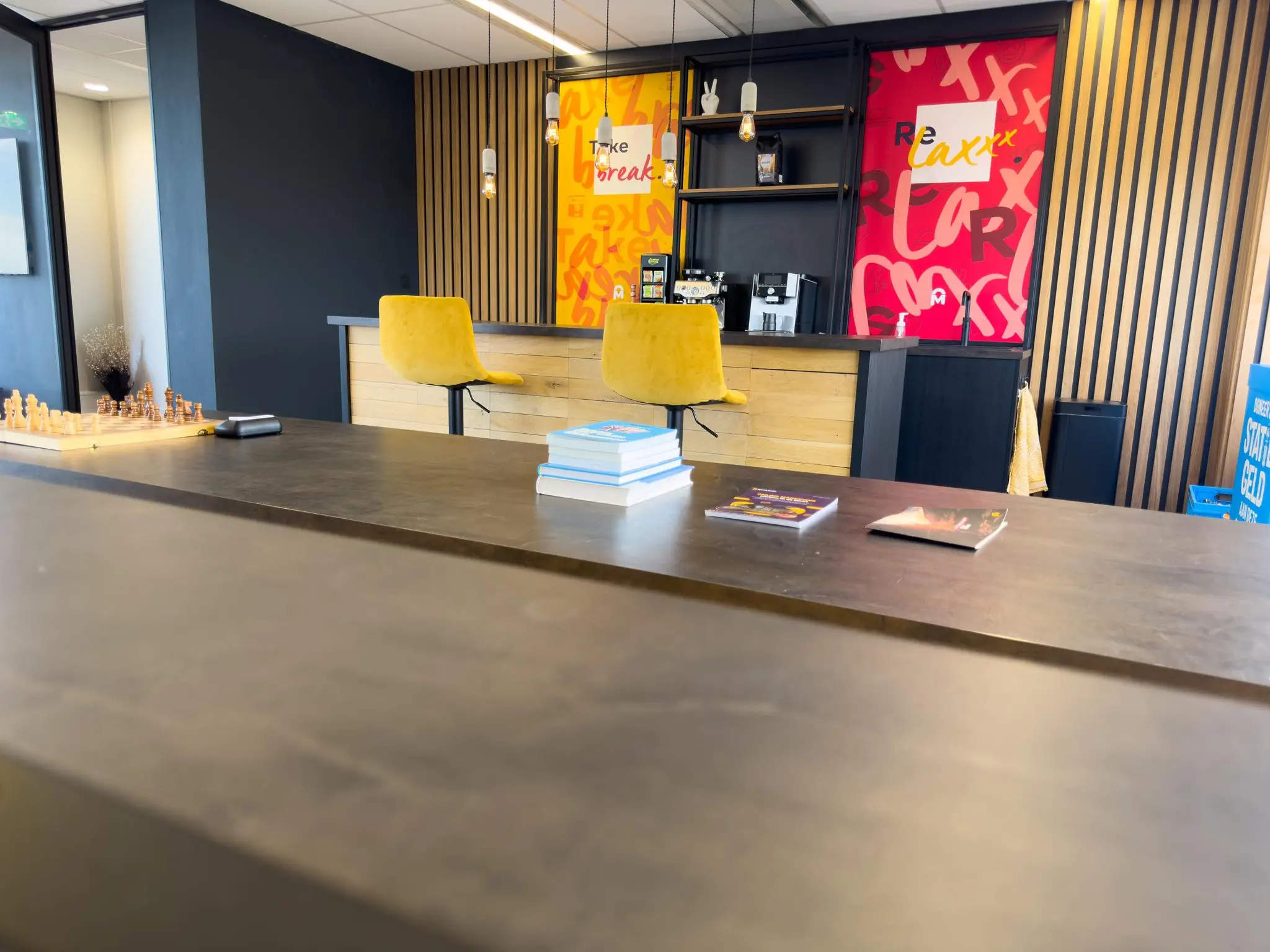 Moderne koffiehoek met gele barkrukken, boeken en een schaakbord in een recreatieruimte aan de Rijnzathe.
