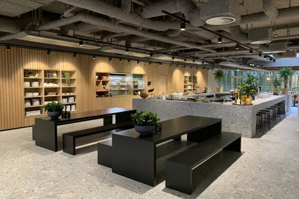 Moderne bedrijfskantine in Rijnzathe met strakke zwarte zitbanken, een open keuken en houten wandbekleding.