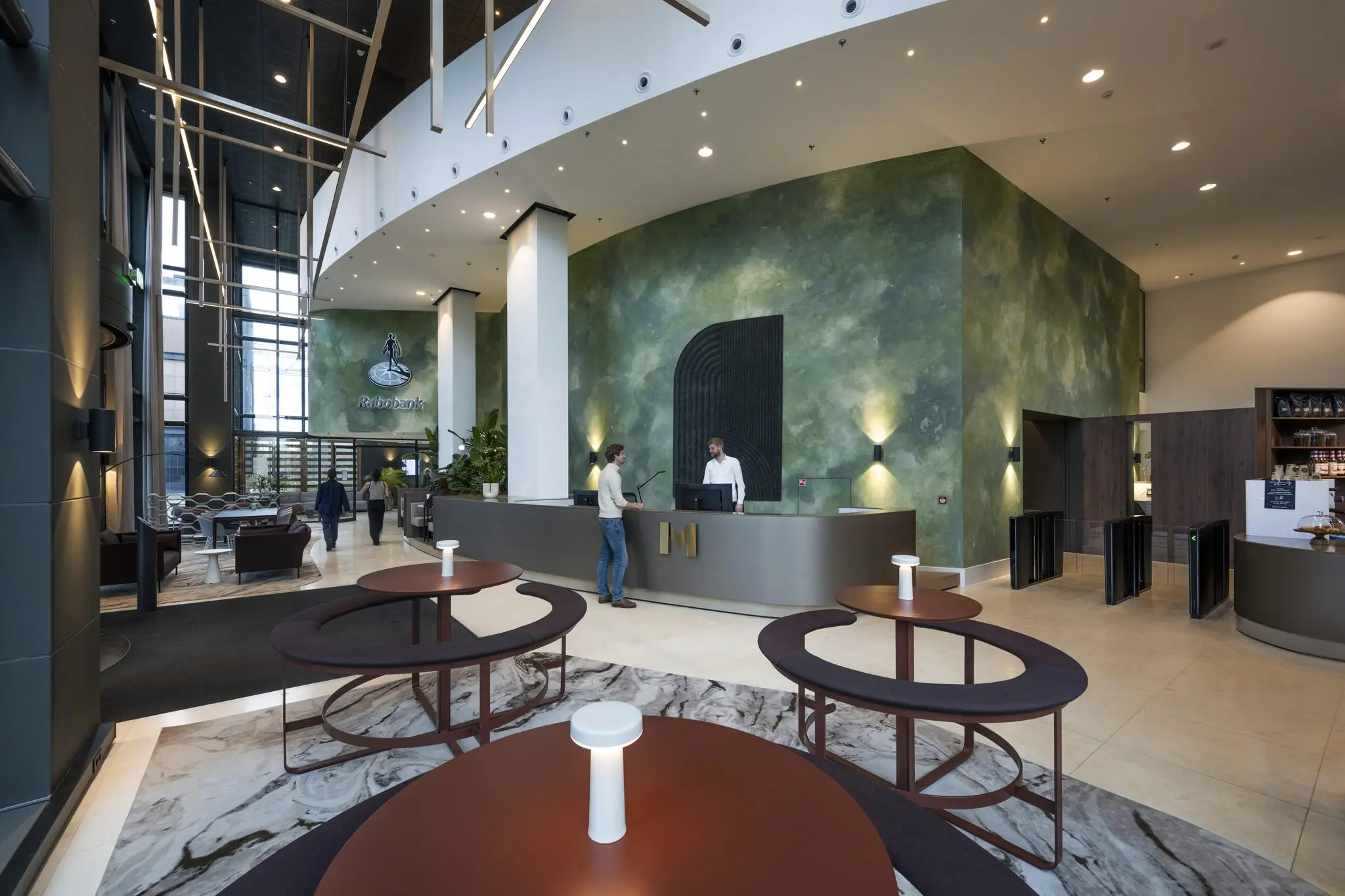 Moderne ontvangsthal van het Rabobank-gebouw aan het Amstelplein met balie, zitgedeelte en groene accentmuur.