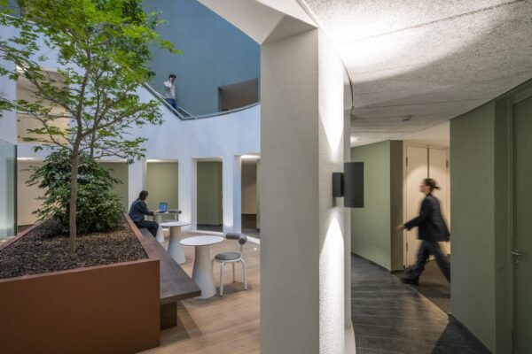 Moderne, open binnenruimte op Amstelplein met binnentuin, zitplekken en mensen in een werkomgeving.