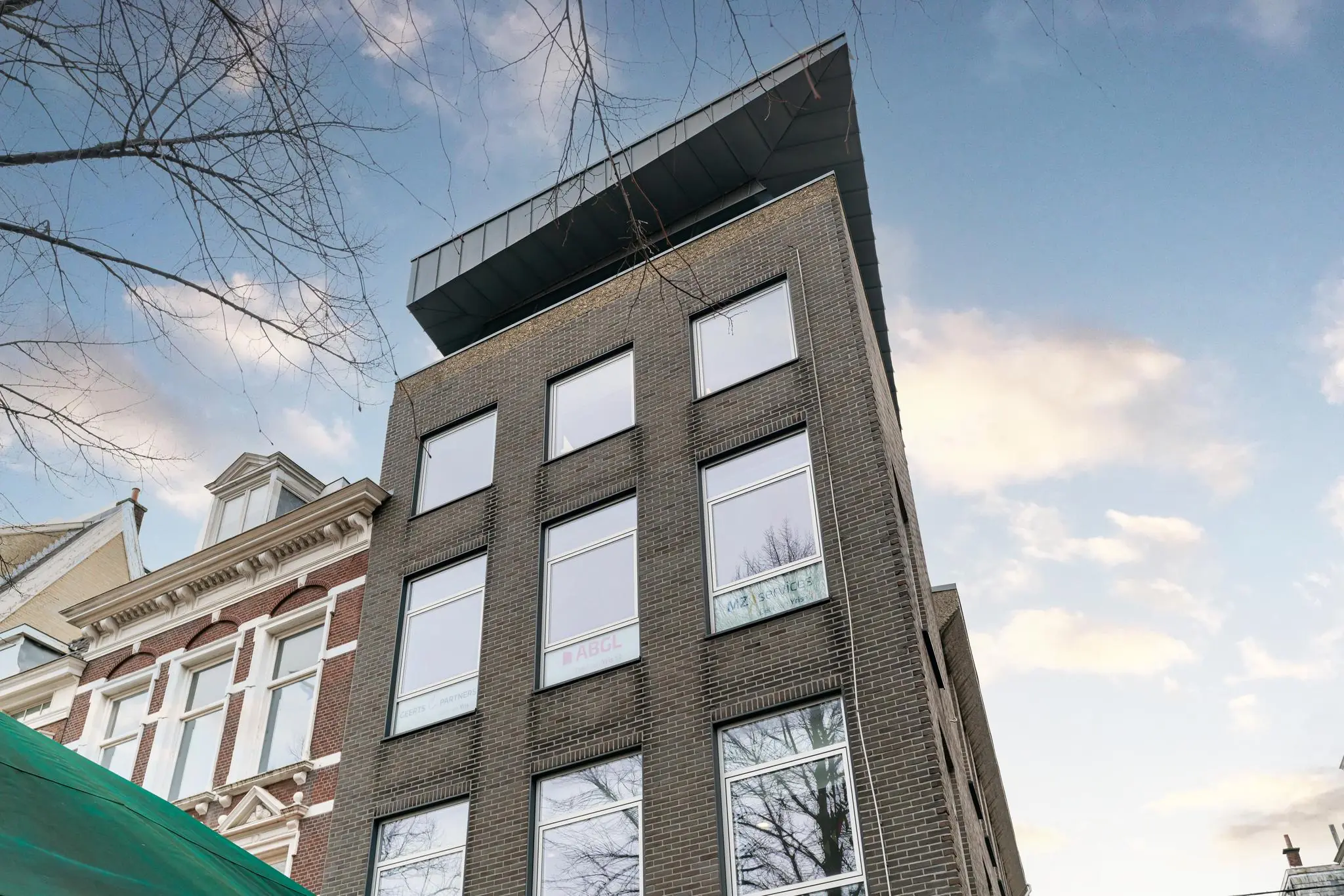 Modern kantoorgebouw aan het plein met donkere bakstenen gevel en grote ramen tegen een blauwe lucht.