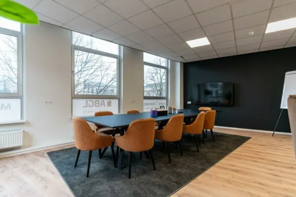 Moderne vergaderruimte met oranje stoelen, een lang zwarte tafel, een flatscreen en zicht op ramen met het logo van ABC Logic.
