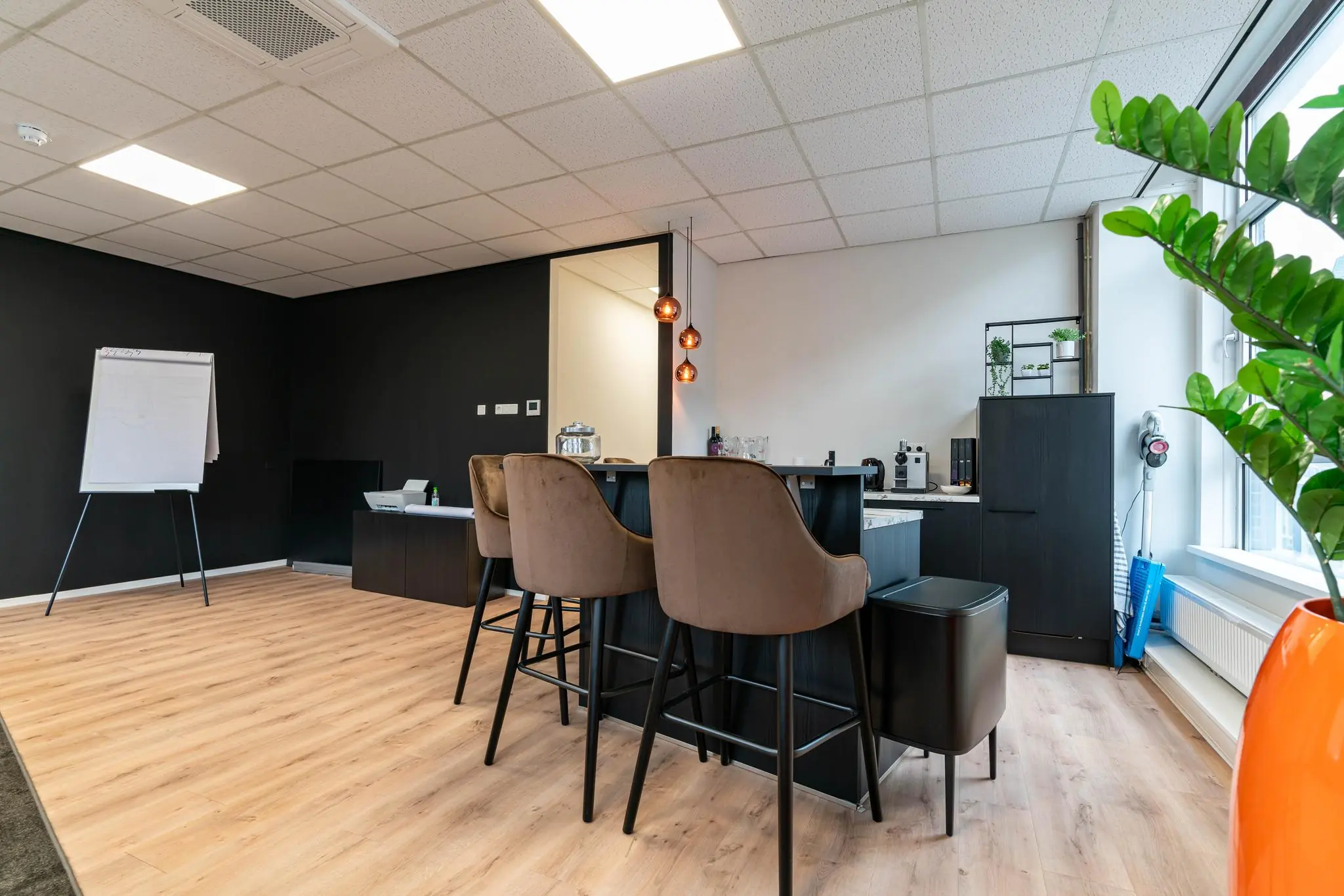Moderne kantoorruimte met een zithoek, barstoelen, een flip-over en een kitchenette met koffieapparaten.