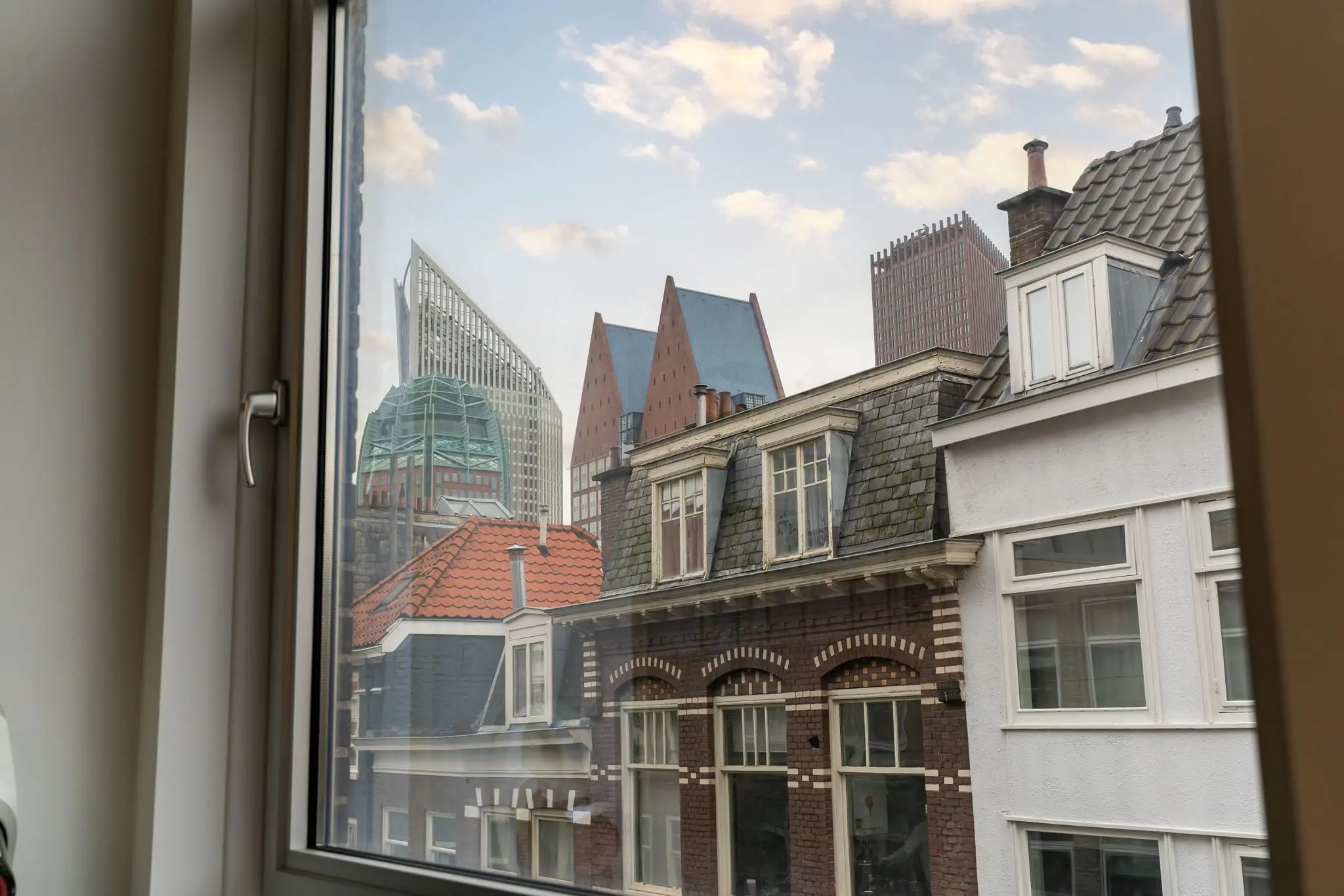 Uitzicht vanuit een raam op historische gevels en moderne hoogbouw aan het Plein in Den Haag.