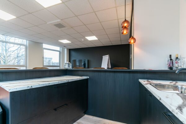 Moderne kantoorruimte met een open kitchenette, marmeren aanrechtbladen en een vergadertafel op de achtergrond.