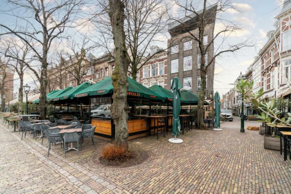 Terras met groene parasols van café Leopold op een leeg plein met klinkerstraat en omringende historische panden.