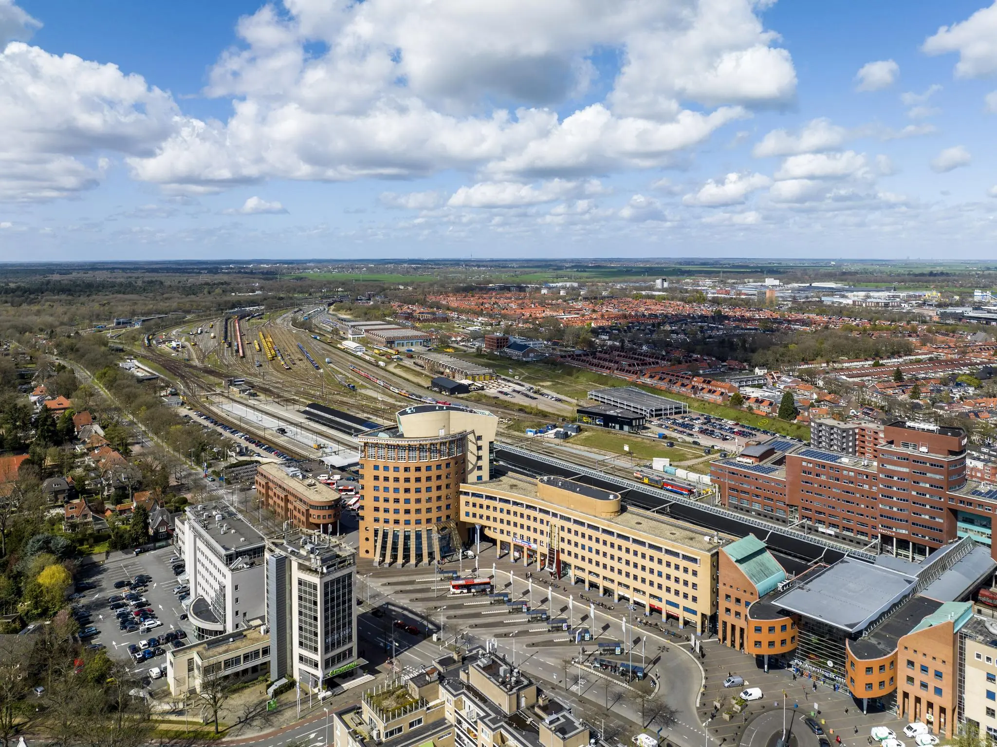Luchtfoto van het Stationsplein in Amersfoort met het station, omliggende kantoorgebouwen en spoorlijnen.