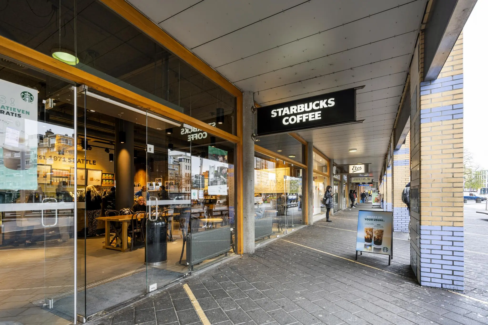 Overdekt winkelgebied aan het Stationsplein met een Starbucks Coffee en andere winkels zoals Etos en Julia’s.