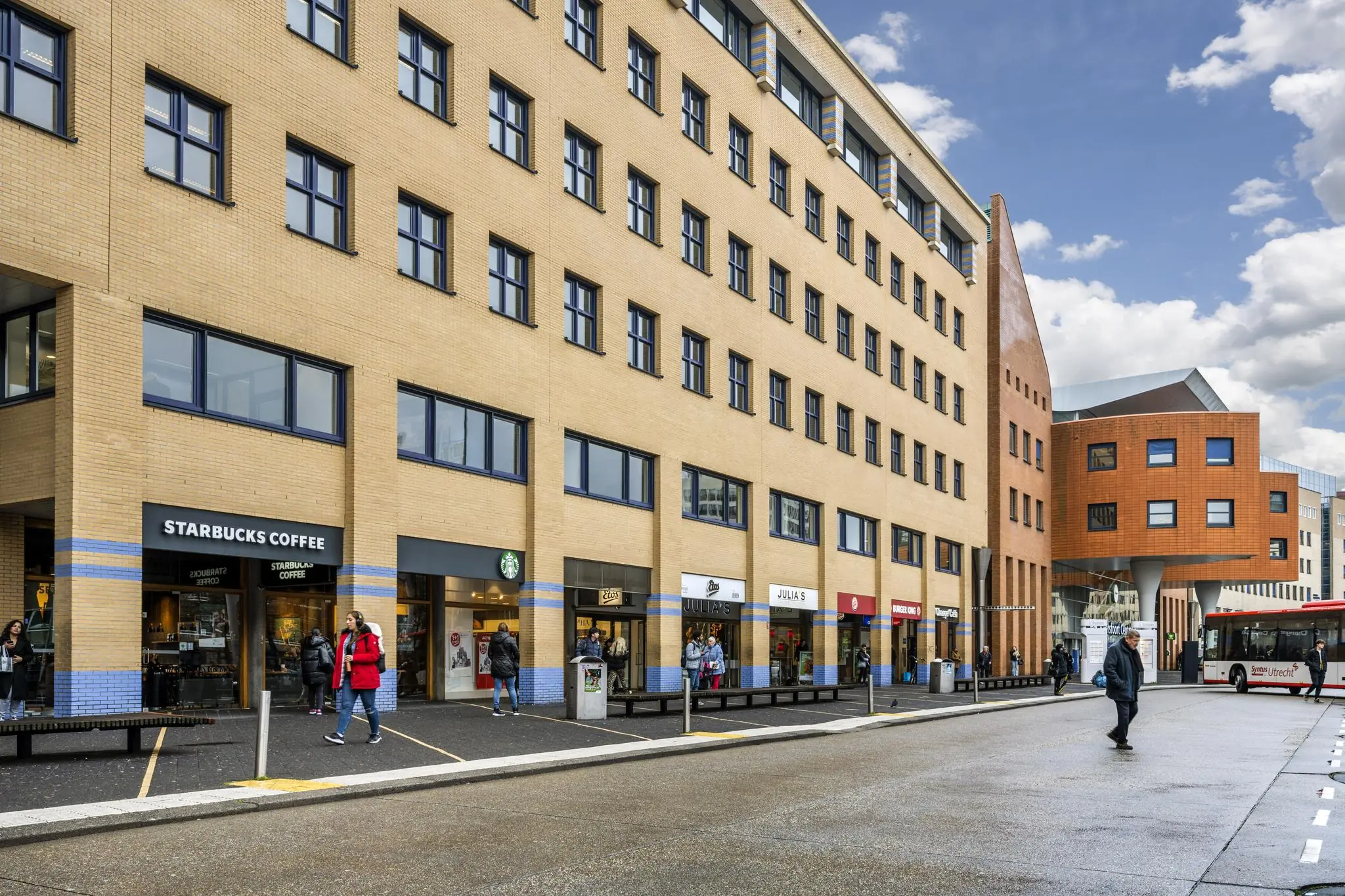 Winkelstraat aan het Stationsplein met onder andere Starbucks, Julia’s en een rood-witte stadsbus op de achtergrond.