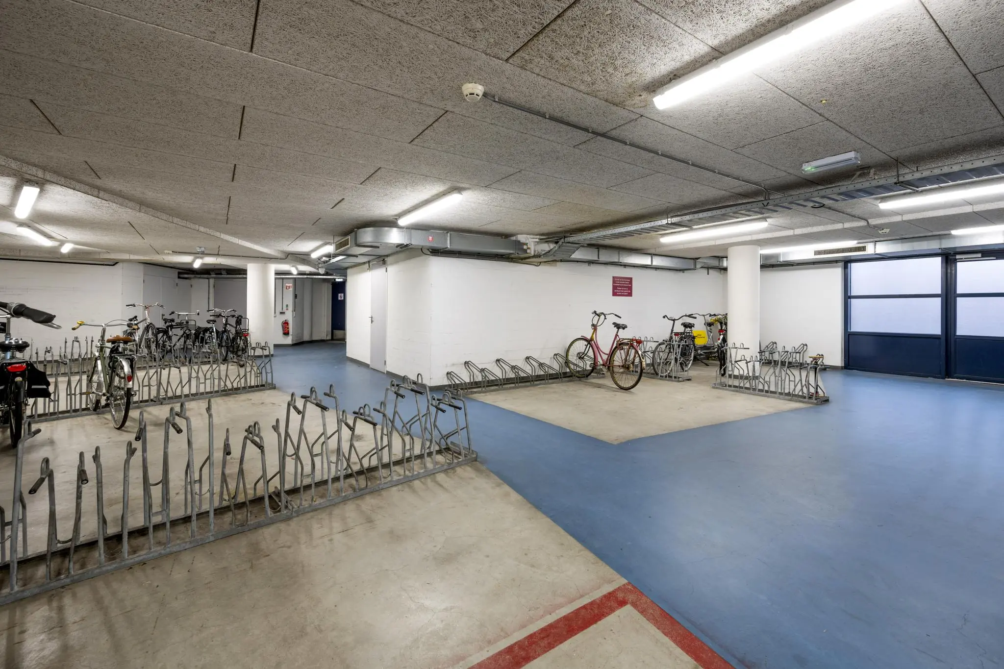 Overdekte en goed verlichte fietsenstalling aan het Stationsplein met meerdere fietsenrekken en geparkeerde fietsen.