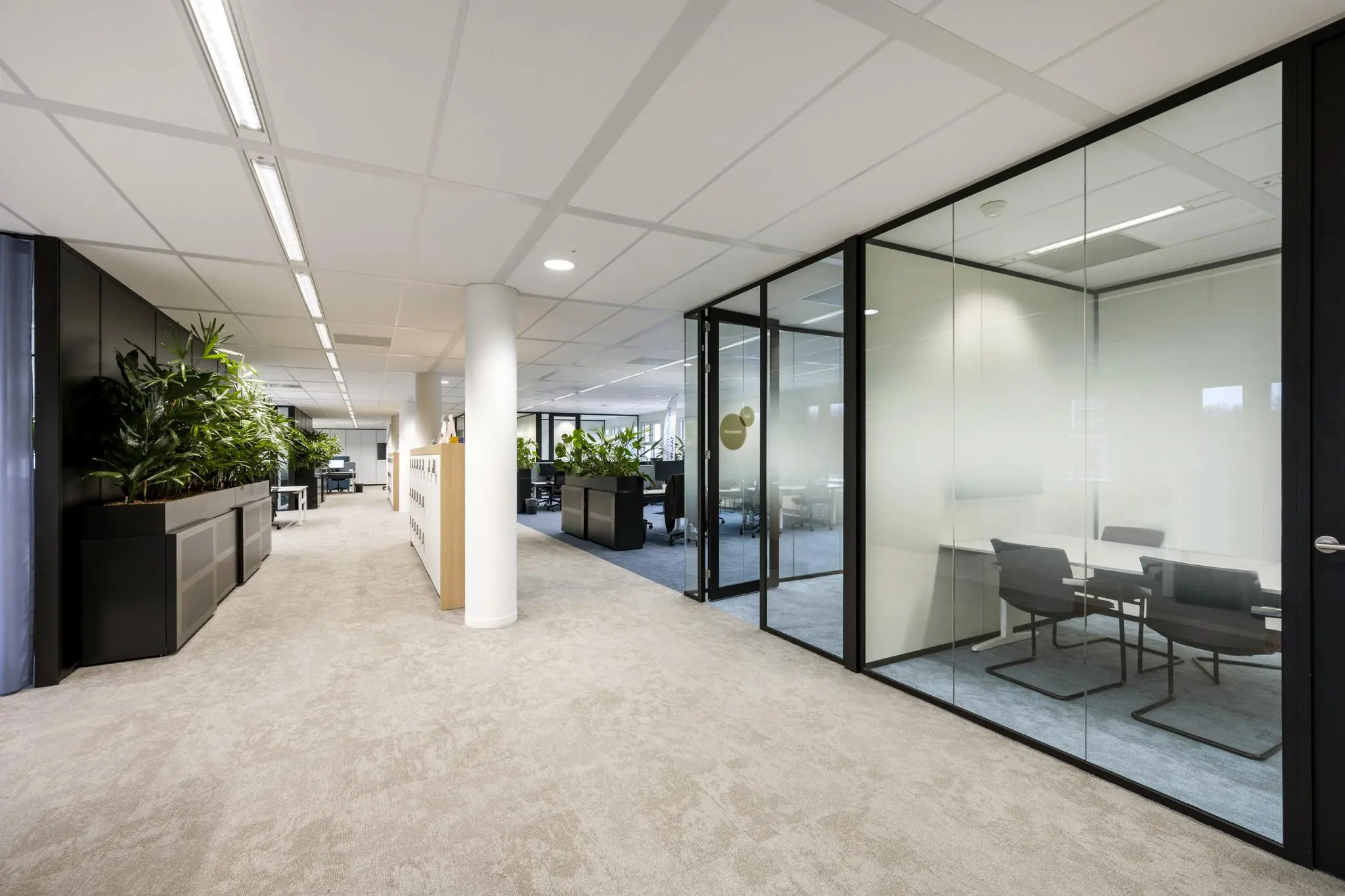 Modern kantoorinterieur aan het Stationsplein met glazen vergaderruimtes, open werkplekken en veel groen.