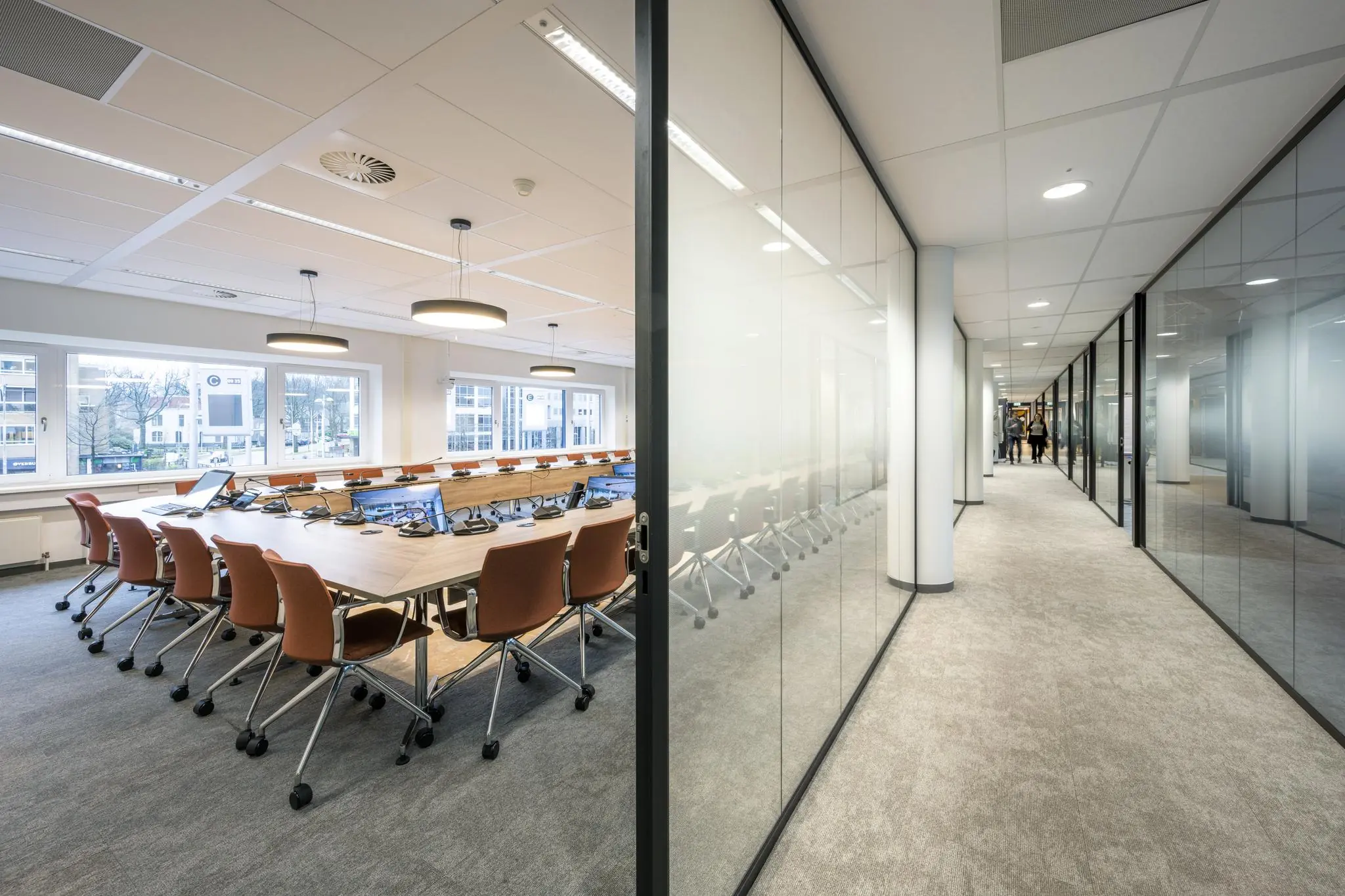 Moderne vergaderruimte met lange tafel en apparatuur, grenzend aan een glazen kantoorgang in het gebouw aan het Stationsplein.