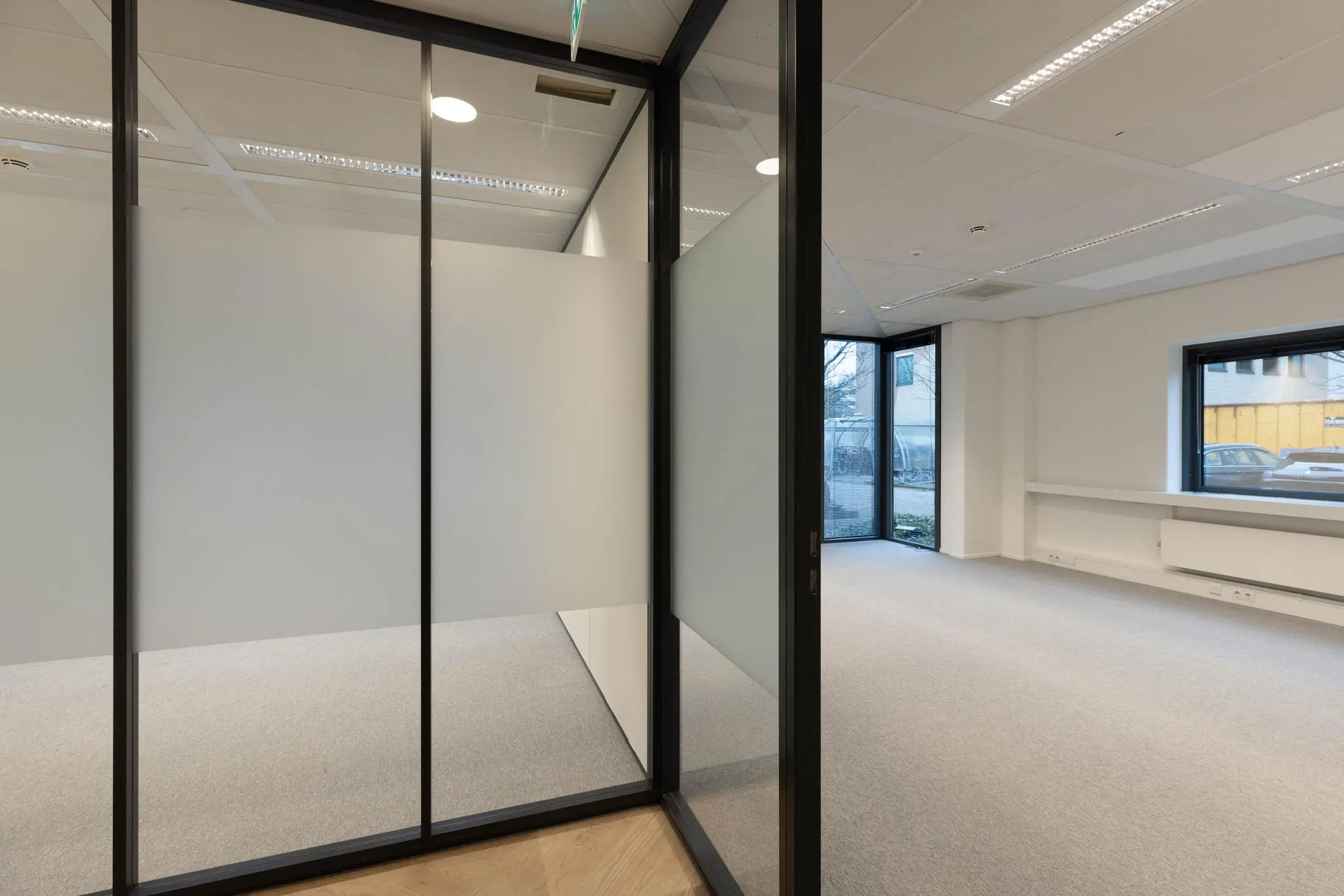 Leeg, modern kantoor met glazen wanden en uitzicht op een parkeerplaats buiten.