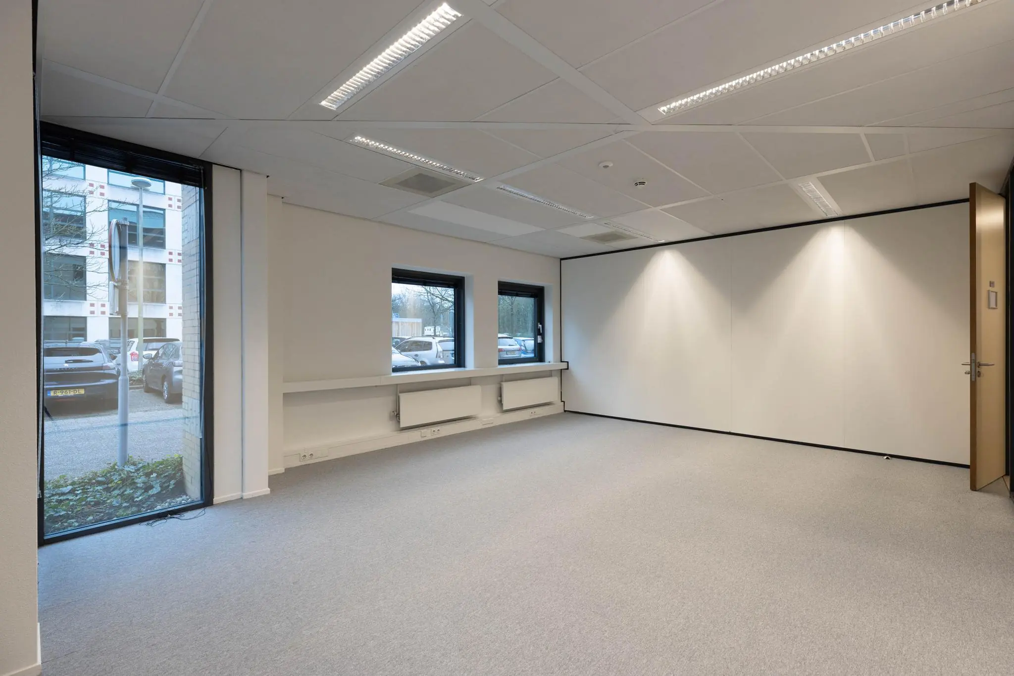Lege, moderne kantoorruimte met vloerbedekking, witte muren en ramen met uitzicht op geparkeerde auto's bij Marathon 175 in Amsterdam.