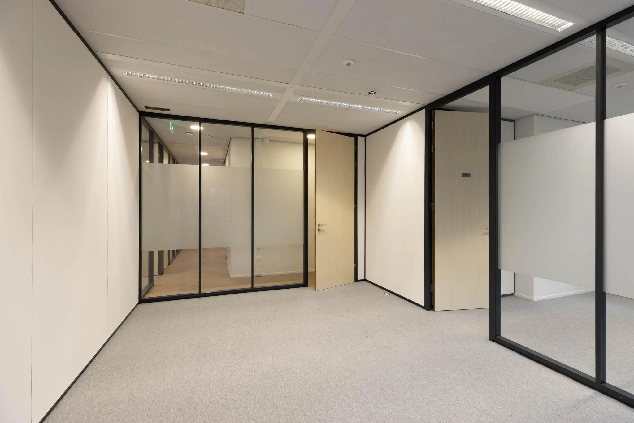 Lege kantoorruimte met glazen wanden, deels matte beglazing en licht houten deuren.