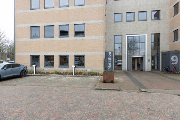 Voorgevel van het kantoorgebouw Marathon met huisnummer 9, voorzien van laadpalen, entree en geparkeerde voertuigen.