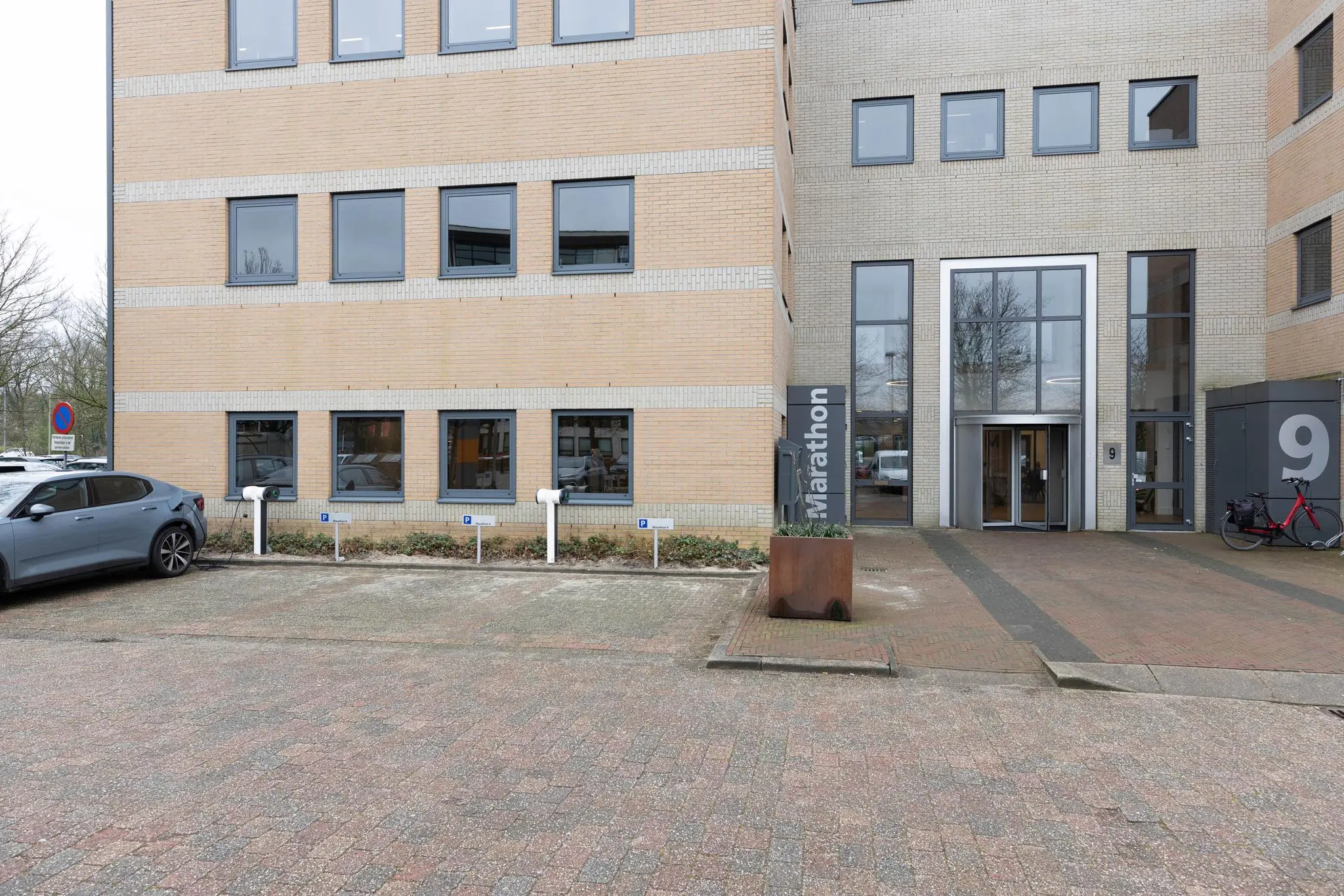 Voorgevel van het kantoorgebouw Marathon met huisnummer 9, voorzien van laadpalen, entree en geparkeerde voertuigen.
