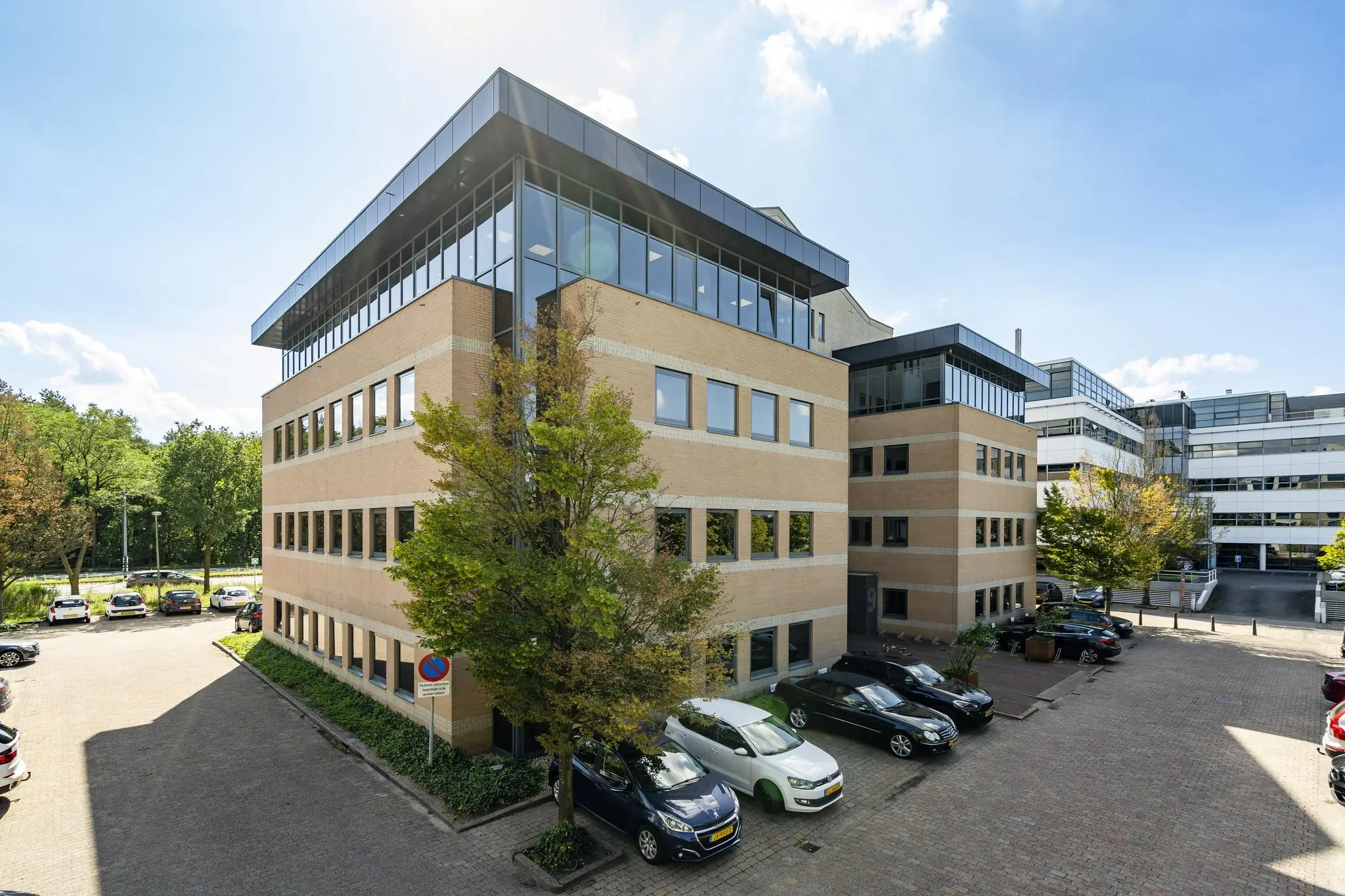 Kantoorgebouw Marathon met parkeerplaatsen en omliggende bomen op een zonnige dag.