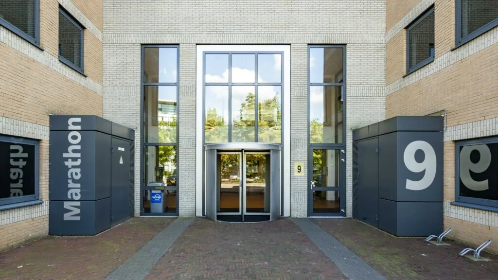 Ingang van het kantoorgebouw Marathon met huisnummer 9 en een draaideur tussen hoge ramen.