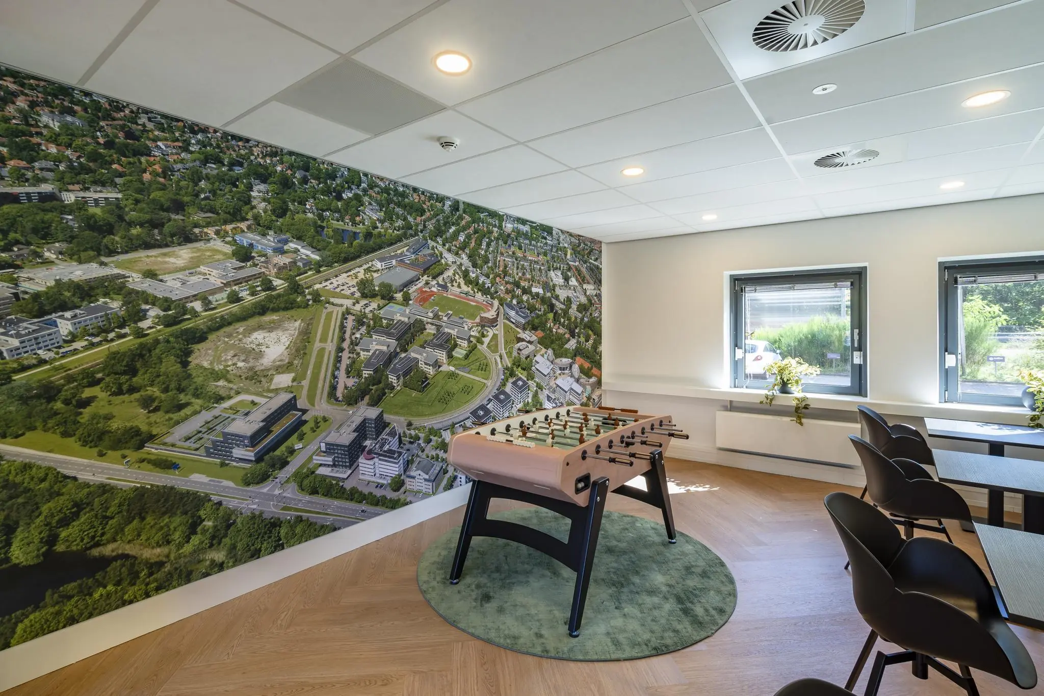 Moderne ontspanningsruimte met een tafelvoetbaltafel en een muurdecoratie van een luchtfoto van bedrijventerrein Marathon in een kantooromgeving.