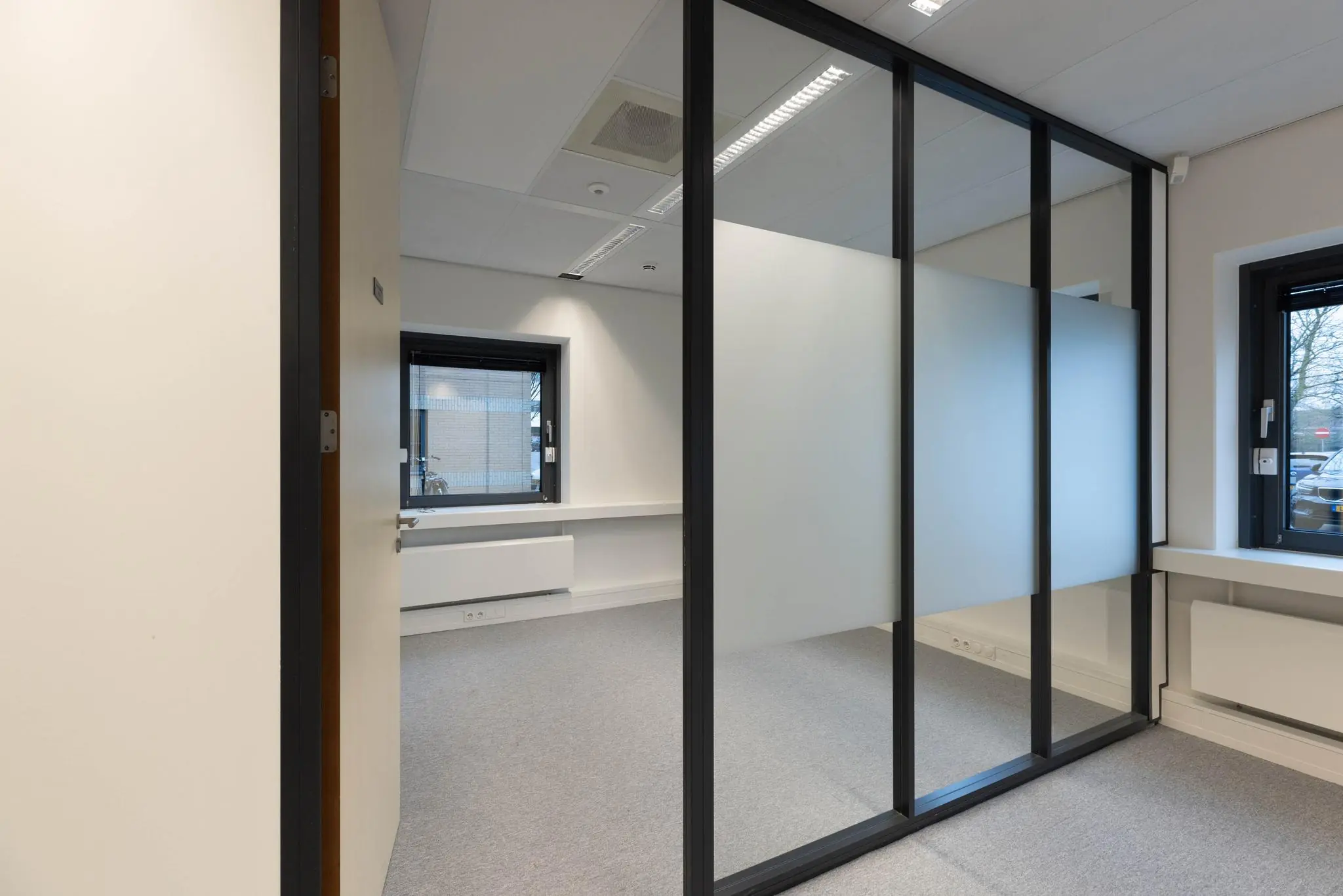 Leeg modern kantoor met glazen scheidingswand en twee ramen met uitzicht naar buiten.