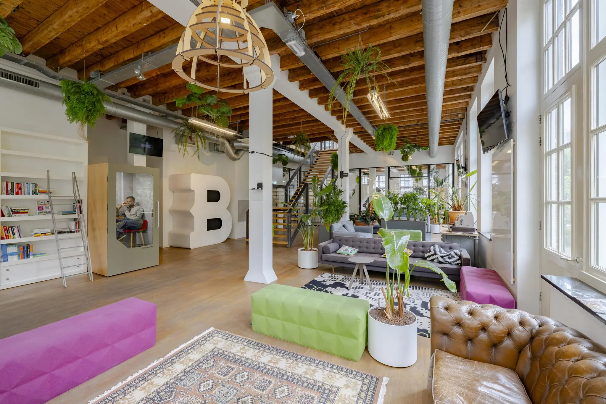 Modern en ruim kantoorinterieur aan de Plantage Middenlaan met veel planten, houten plafond en kleurrijk meubilair.