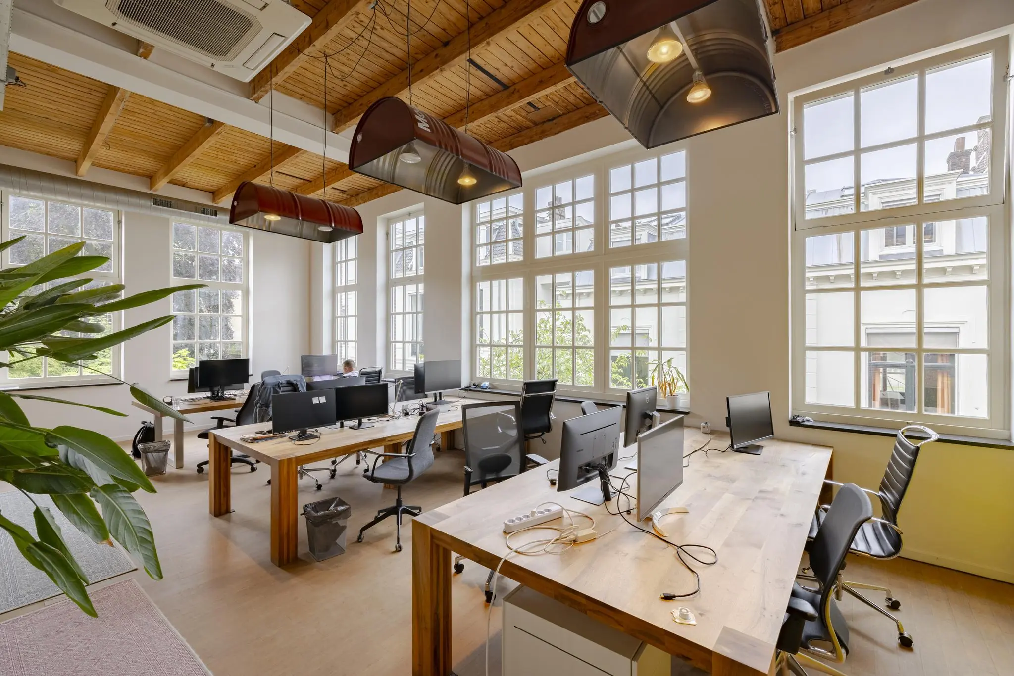 Licht en modern kantoorinterieur aan de Plantage Middenlaan met grote ramen, houten plafond en werkplekken met computers.