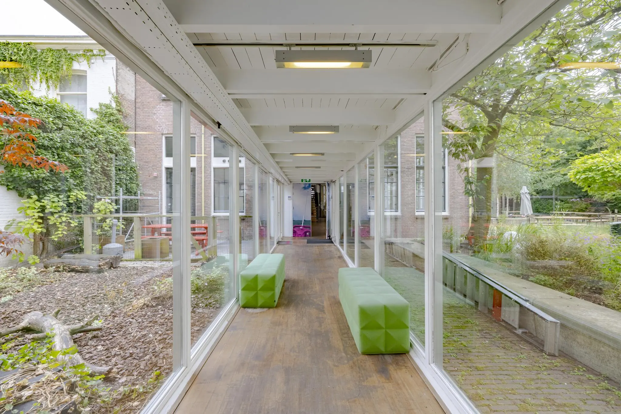 Overdekte glazen gang met groene banken en uitzicht op binnentuinen aan de Plantage Middenlaan.