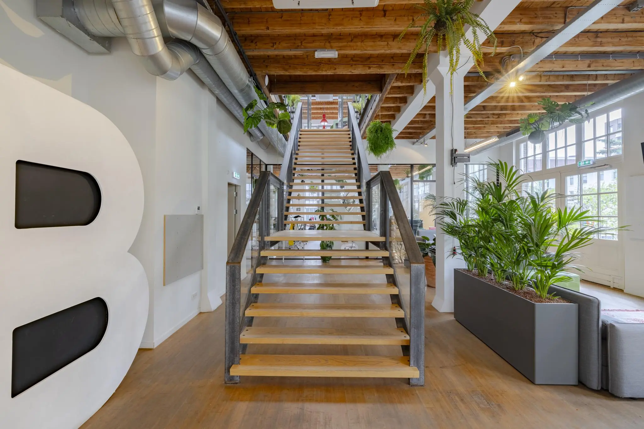 Houten trap in een modern industrieel interieur aan de Plantage Middenlaan, omringd door planten en glazen wanden.