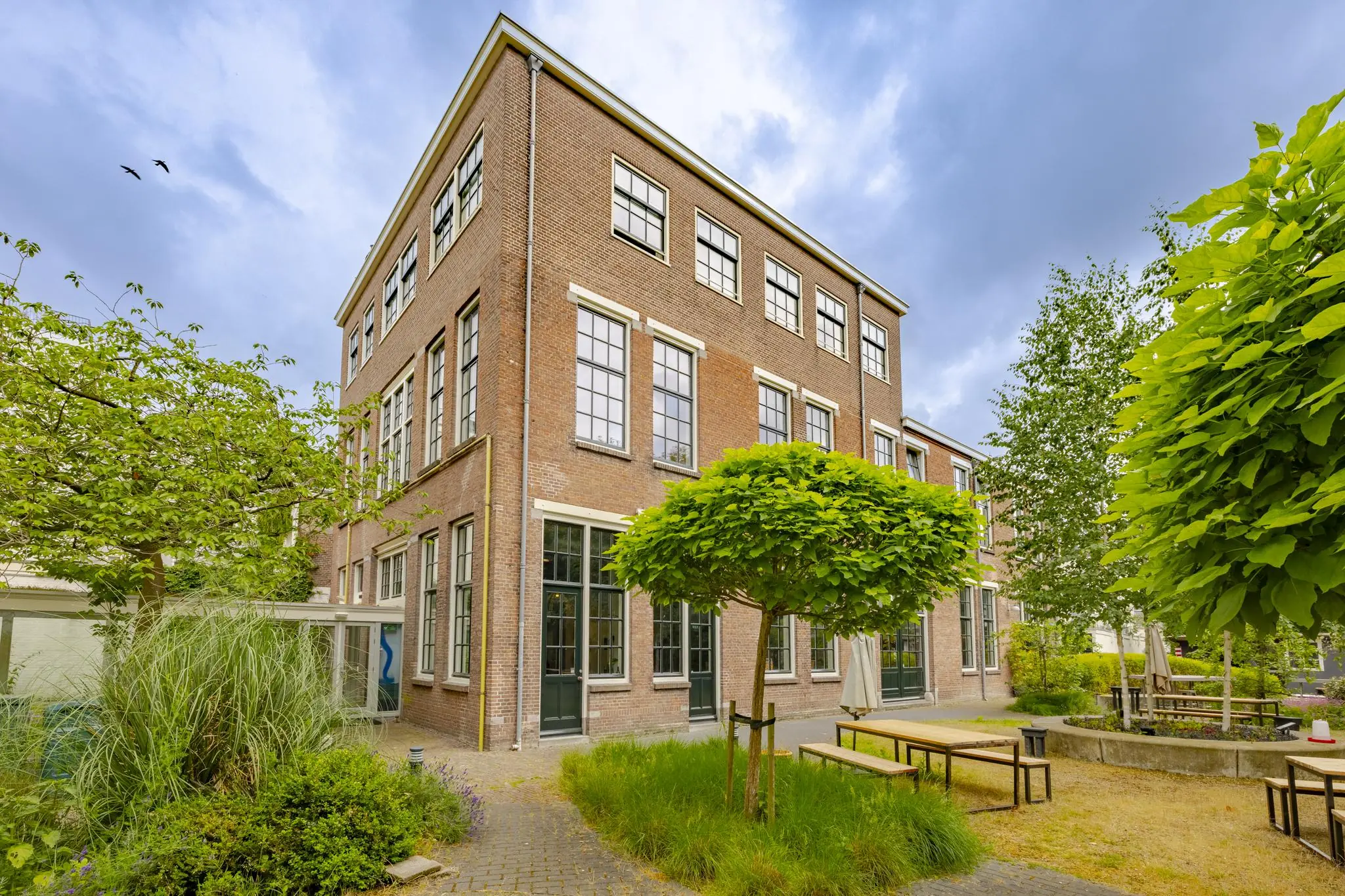 Binnenplaats met zitbanken en groene begroeiing bij een historisch bakstenen pand aan de Plantage Middenlaan.