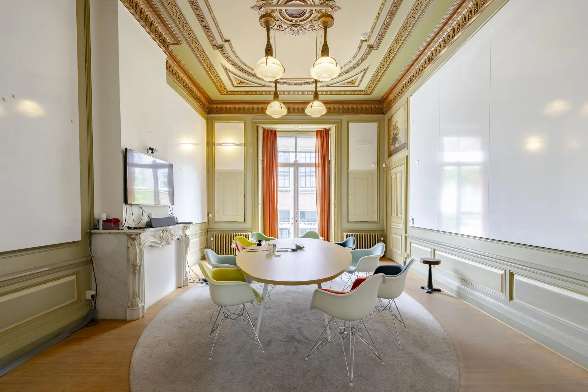Vergaderkamer aan de Plantage Middenlaan met een ovaal houten tafel, moderne stoelen, een sierlijk plafond en een groot scherm boven een marmeren schouw.