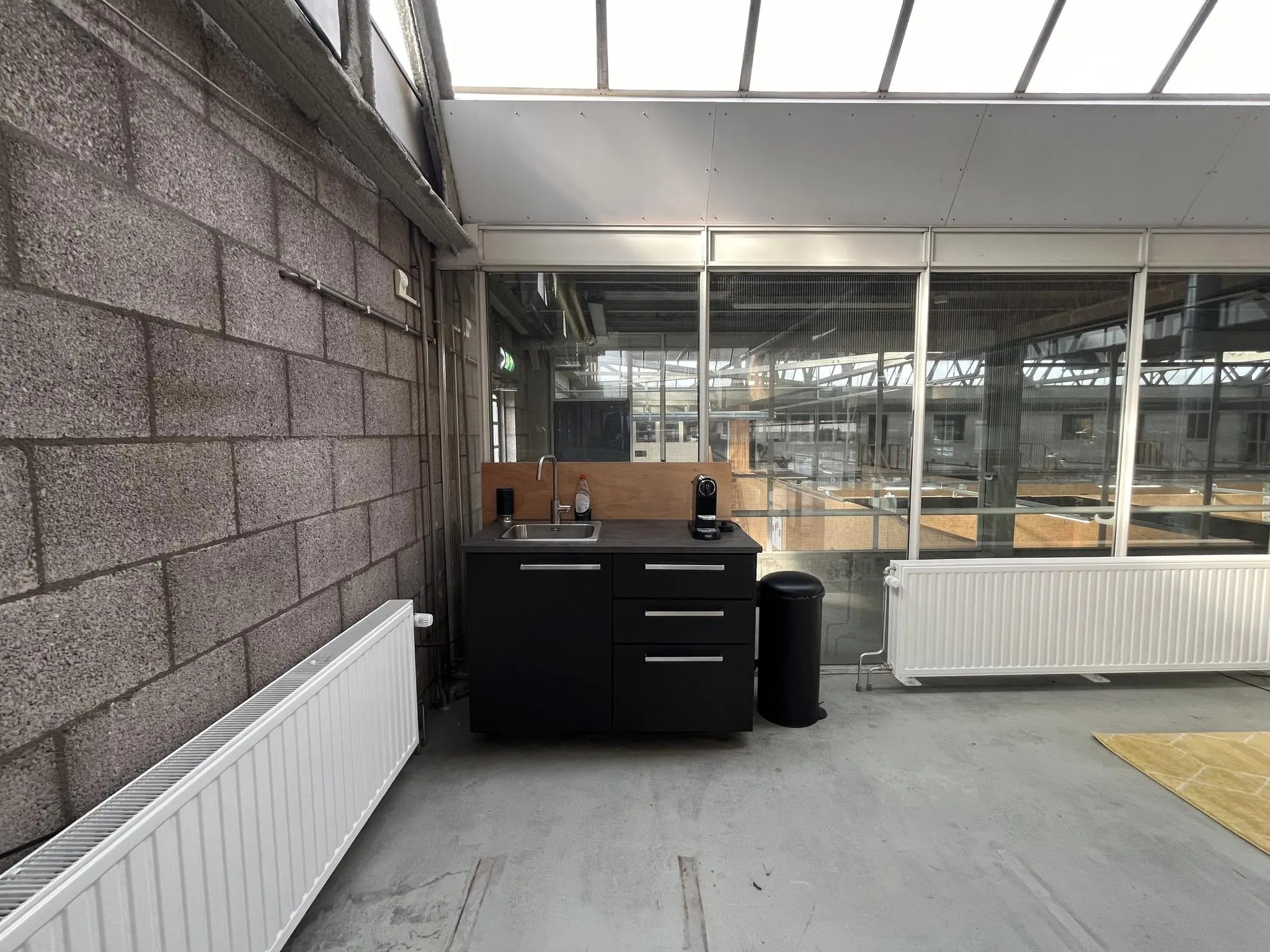 Kleine pantry met zwarte keukenkastjes en koffiezetapparaat in een industriële ruimte aan de Eendrachtlaan.
