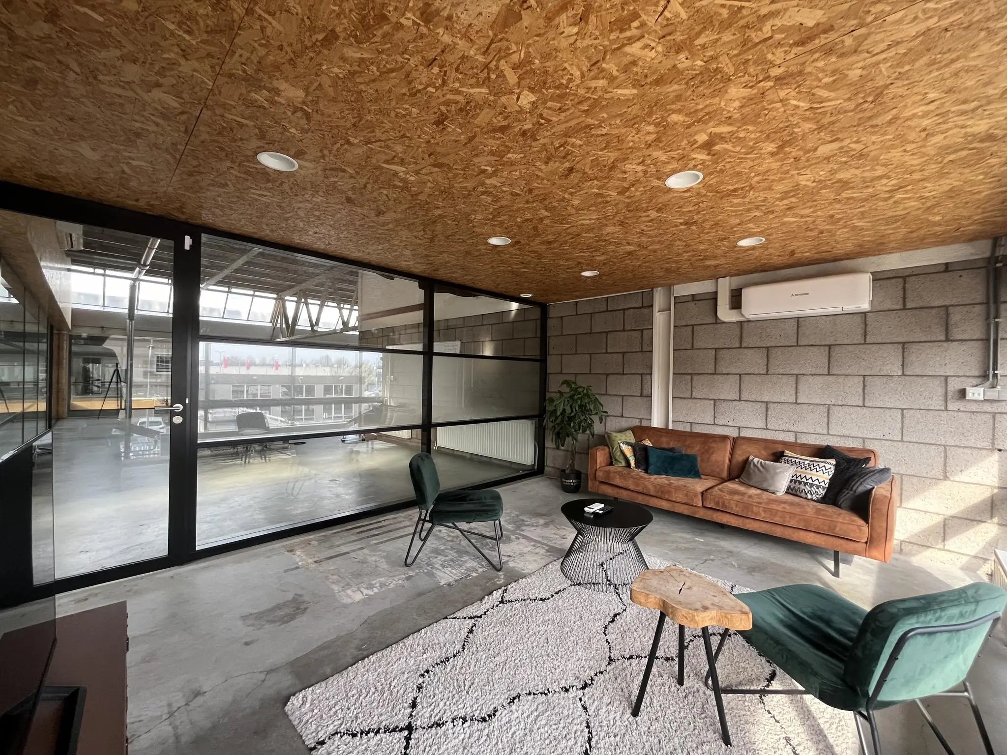 Moderne wachtruimte aan de Eendrachtlaan met een leren bank, designstoelen en een glazen wand die uitzicht biedt op een vergaderruimte.