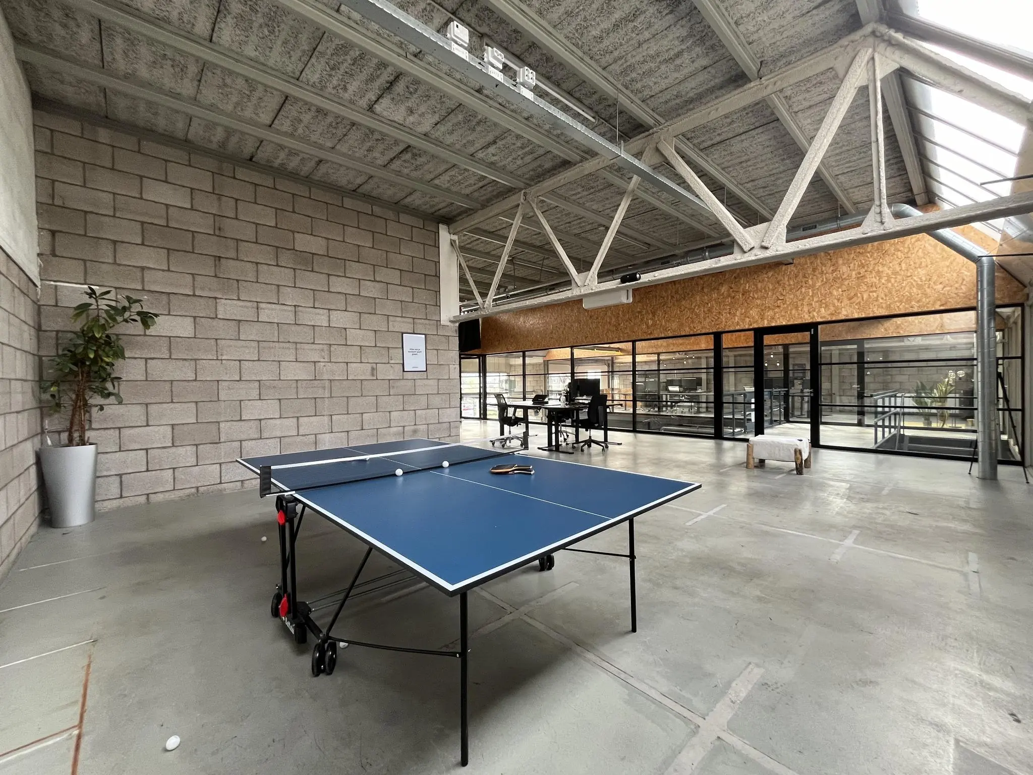 Moderne kantoorruimte aan de Eendrachtlaan met een pingpongtafel op een betonnen vloer en glazen vergaderruimtes op de achtergrond.