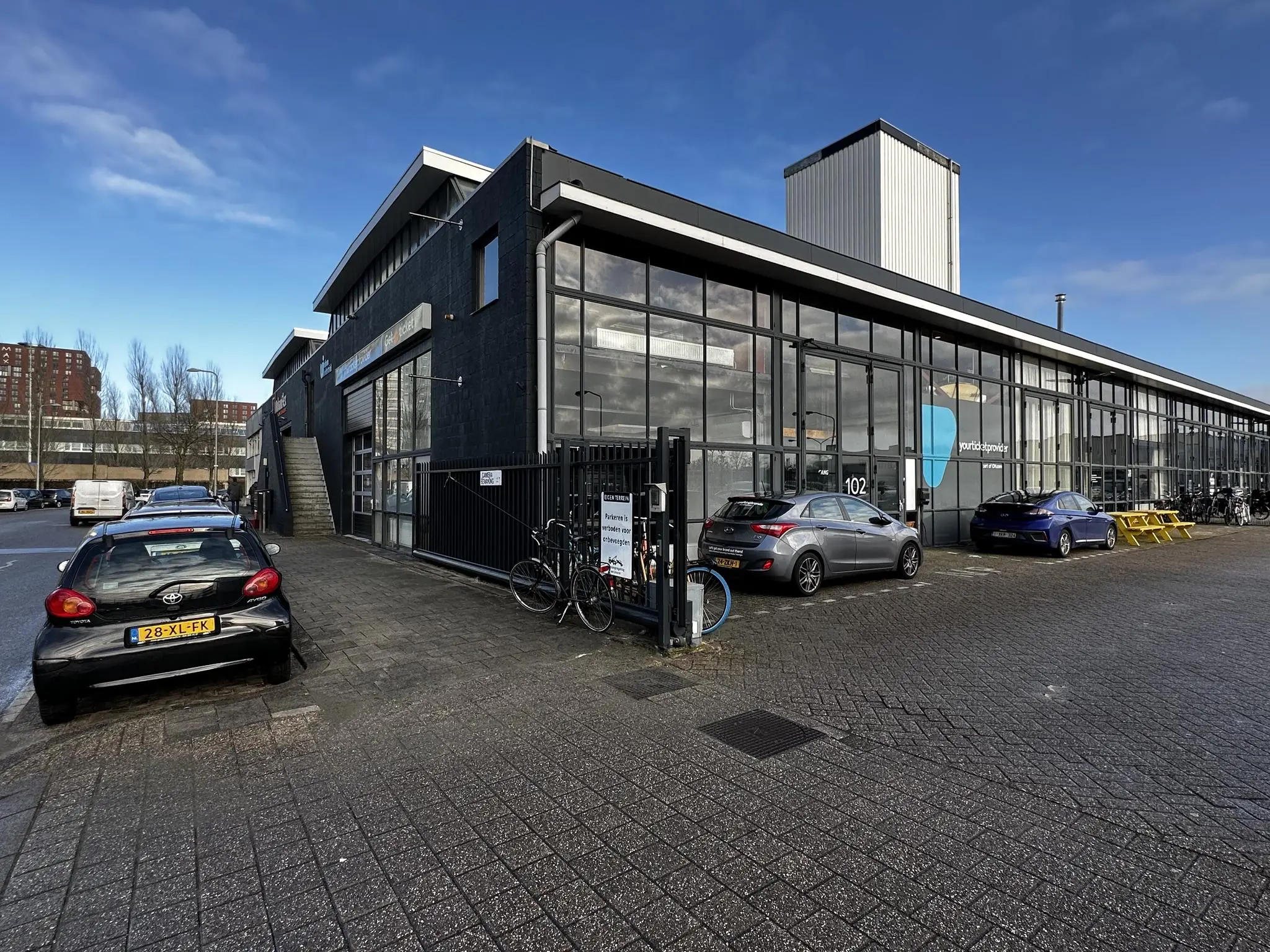 Bedrijfsverzamelgebouw aan de Eendrachtlaan met geparkeerde auto's en fietsen op een zonnige dag.