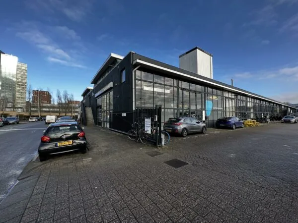 Bedrijfsverzamelgebouw aan de Eendrachtlaan met geparkeerde auto's en fietsen onder een blauwe lucht.