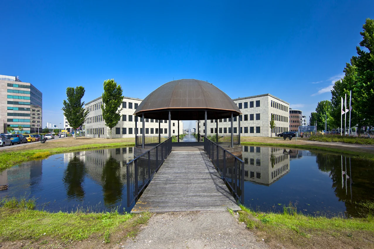 Een houten brug met overkapping over een vijver bij kantoorgebouwen aan de Rivium 1e Straat in een zakendistrict.