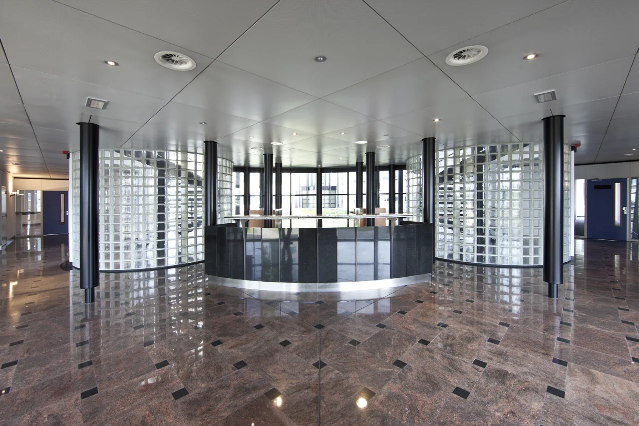 Moderne ontvangsthal met glanzende marmeren vloer, glazen bouwstenen en een ronde balie aan de Rivium 1e Straat.