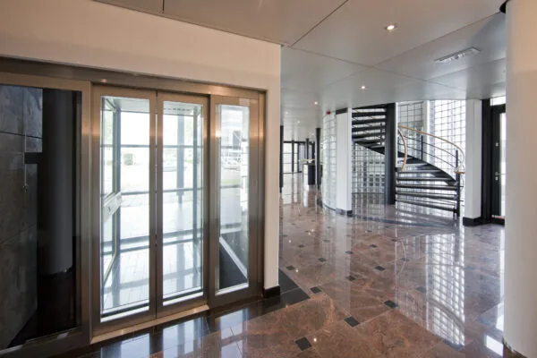 Moderne entreehal aan de Rivium 1e Straat met een glazen lift en een zwart metalen wenteltrap.