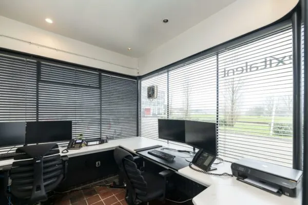 Kantoorruimte aan de Lindtsedijk met werkplekken, computerschermen, telefoons en uitzicht naar buiten door jaloezieën.