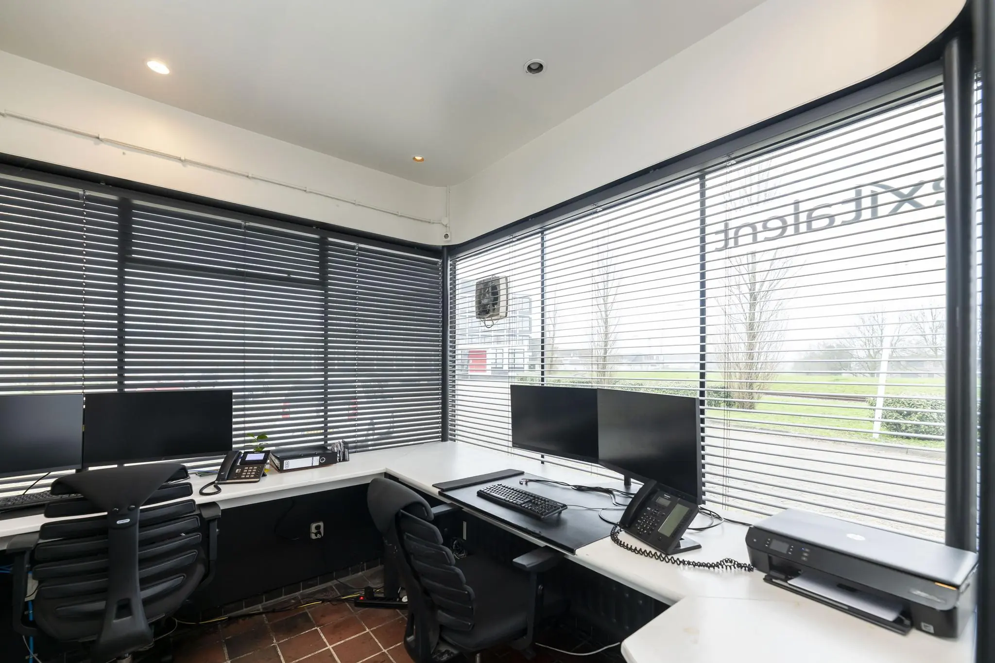 Kantoorruimte aan de Lindtsedijk met werkplekken, computerschermen, telefoons en uitzicht naar buiten door jaloezieën.