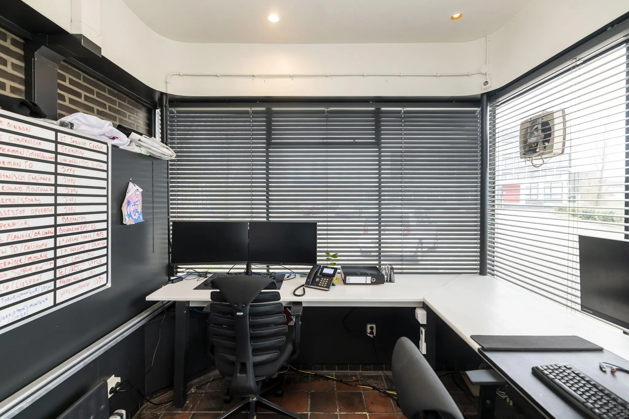 Kantoorruimte aan de Lindtsedijk met werkplekken, computers, jaloezieën en een whiteboard met planning.