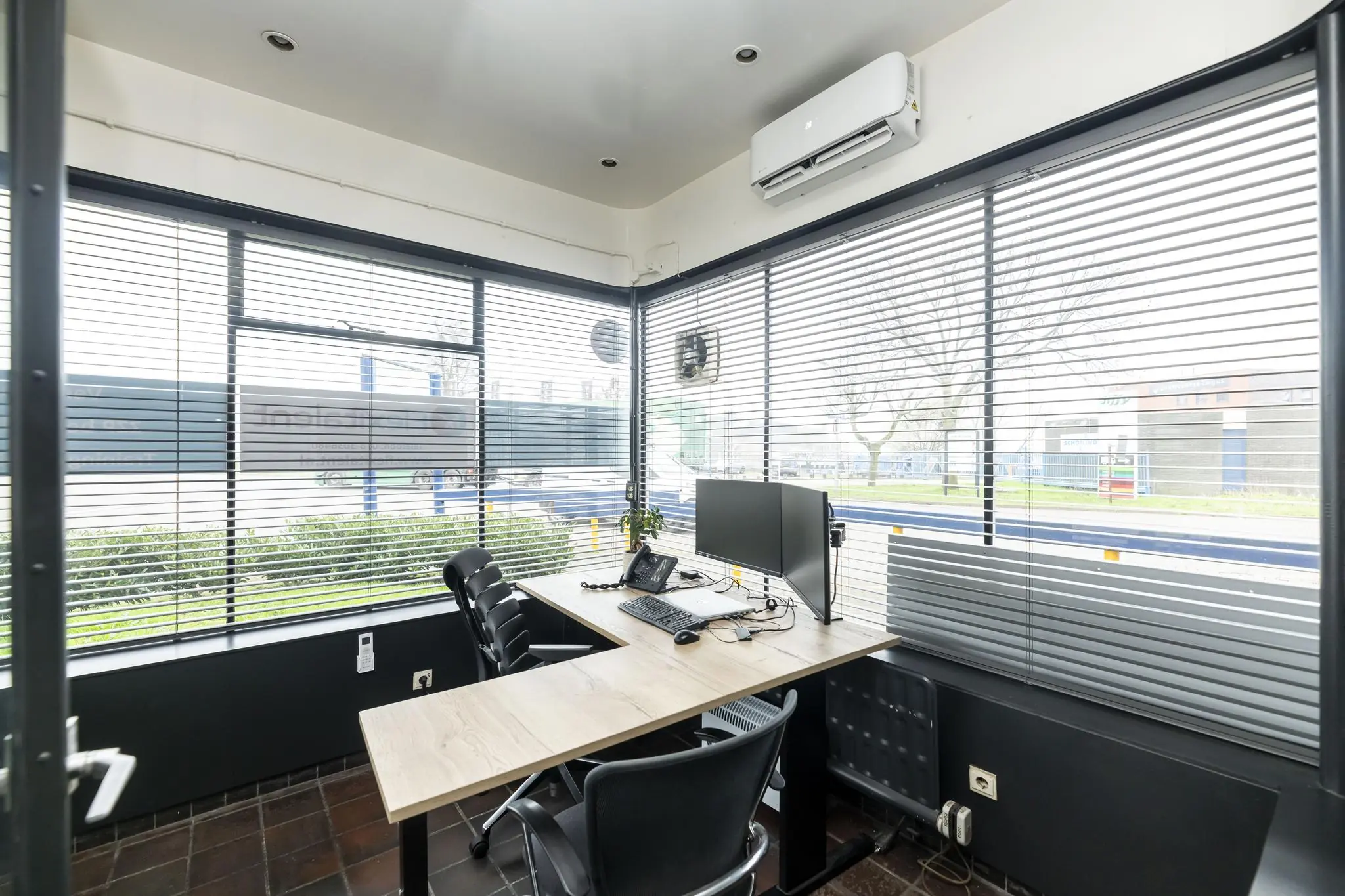 Modern kantoor met een hoekbureau, dubbele monitoren en grote ramen met jaloezieën aan de Lindtsedijk.