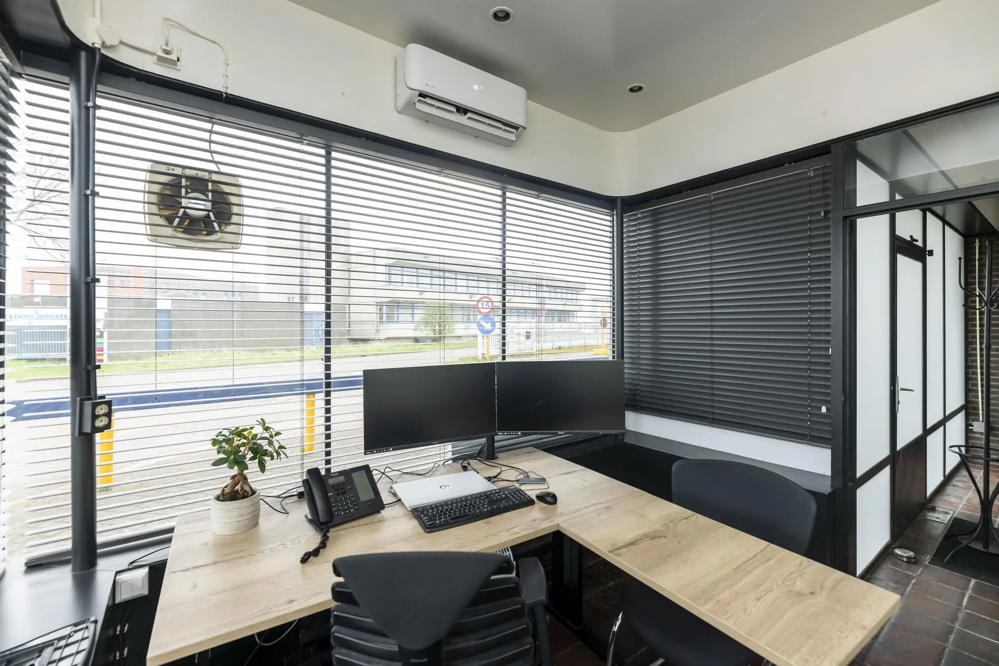 Modern kantoor met houten bureau, dubbele monitoren, een laptop en raamjaloezieën aan de Lindtsedijk.